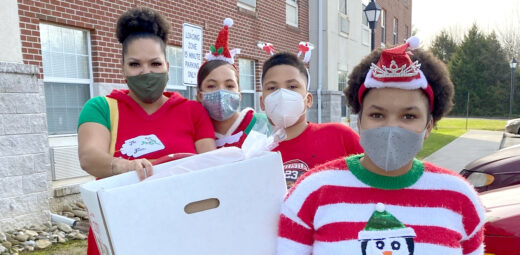 A mom and her children wearing festive outfits and masks deliver food to residents