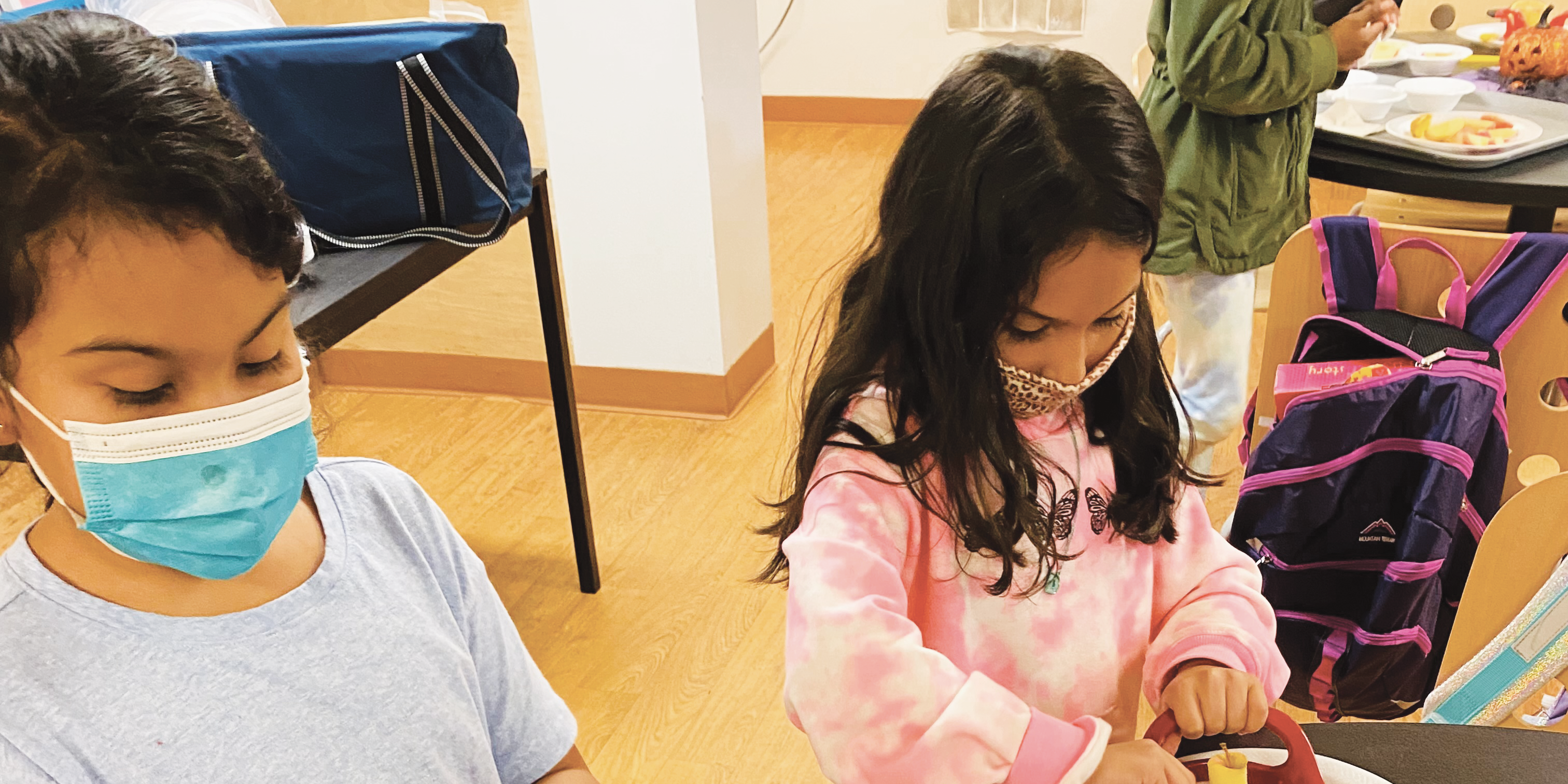 Two children are making apple nachos on a table at a Mercy Housing building.