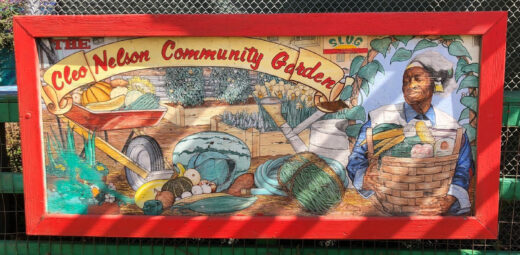 A photo of a hand painted sign, with a garden mural and a man holding a basket of vegetables, with the title "Cleo Neslon Community Garden"