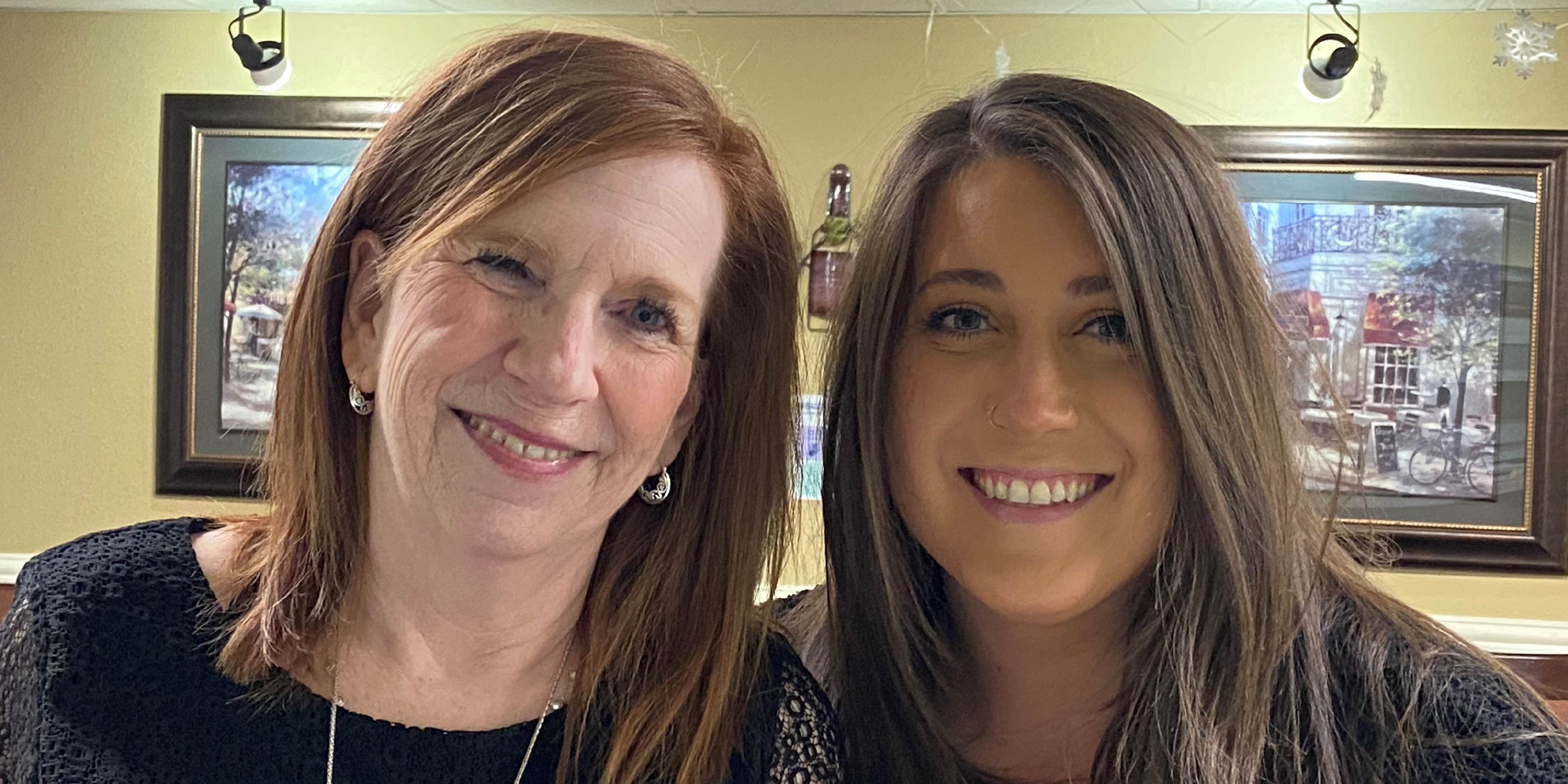 A photo of two women volunteers smiling at the camera while volunteering at a food pantry